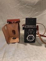 Front view of Lubitel 2 camera beside its leather case