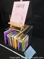 Lot overview with pink 'Crystalline Communion' on easel and paperbacks in acrylic holder