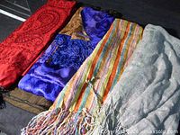 Five folded scarves laid side by side showing colours, patterns and fringe detail