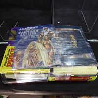 Stack of shrink-wrapped and loose hardcover books showing Anatomy for Fantasy Artists on top and assorted spines including Tolkien