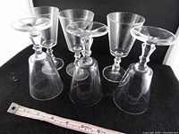 Six clear stemmed cordial glasses, some upright, some inverted, measuring tape showing approx. height