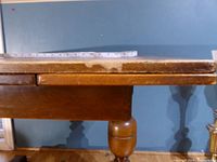 Side view showing tabletop edge, drop-leaf hinge, turned leg, surface wear