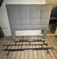 Front view of grey tufted headboard with metal frame pieces laid out