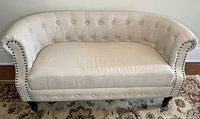Full front view of loveseat showing upholstery, tufting, nailhead trim, and legs