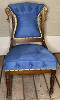 Front view of carved wood chair with blue tufted upholstery and gold trim