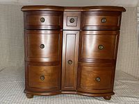 Front view of closed large Bombay & Co. jewelry cabinet showing wood finish and drawer layout.