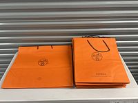 Stack of Hermes orange shopping bags folded and upright on table