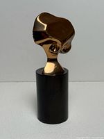 Frontal view of gold-plated bronze head sculpture on black pedestal