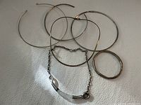 Four thin sterling chokers, chain bracelet, and bangle arranged on white surface