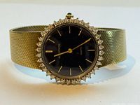 Front view showing black dial, halo bezel with stones, gold-tone mesh bracelet