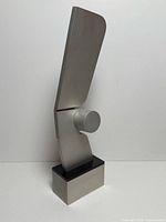 Front view of brushed aluminum abstract sculpture on two-tier base