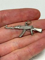 Front view of sterling silver AK-47 pendant resting on fingertip