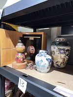 All four pieces on shelf – kokeshi lamp, framed mask, blue-and-white ginger jar, multicolour vase