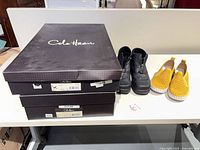 Stacked Cole Haan shoe boxes with black ankle boots and mustard slip-ons visible
