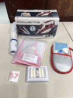 Lot overview showing Rowenta iron box, iron, bath mat roll, pink mesh pads, silver pressing pad, LED light