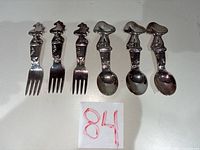 Six infant utensils laid out, three forks and three spoons with character handles