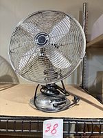 Front view of chrome desk fan showing wire guard, blades, base and control numbers