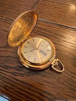 Open pocket watch showing dial marked Birks Quartz with day window