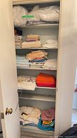 Tall linen closet showing multiple shelves of folded linens including afghans, towels, sheets, mattress covers