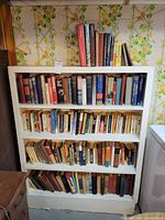 White bookcase with four filled shelves and additional books on top