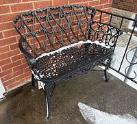 Front view of black cast aluminum bench on porch showing heart motif backrest and openwork seat