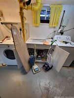 Overall lot view showing Hoover vacuum, Bissell QuickSteamer, ironing board and cabinet of cleaning products