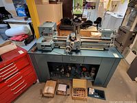 Full view of lathe on cabinet with accessories beneath and boxes of tooling