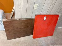 Square red card table top leaning against wall