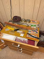 Drawer with assorted tools and materials including coping saw, adhesives, batting, blade packs, strop end visible