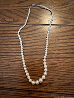 Full view of graduated pearl necklace laid flat on wood surface