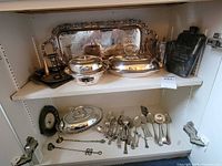 Full view of cabinet shelves with trays, covered dishes, candle holder, flask and flatware