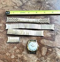 Watch head and three bracelets laid out with tape for scale