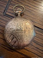 Exterior of closed engraved pocket watch showing monogram and floral pattern