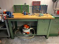 Front view of green steel workbench with hardwood top, mounted Record No.3 vise visible