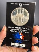 Front view of coin in holder showing design and Olympic graphics
