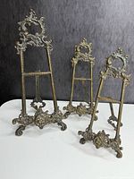 Front view of three bronze plate stands showing size differences and ornate design