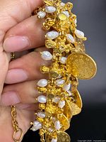 Close-up of necklace showing gold-tone links, freshwater pearls, and coin charms