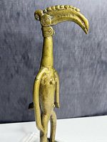 Side profile of bronze tribal figure highlighting beak-like head and spiral ear details