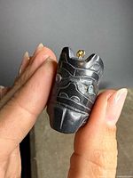 Front view of carved argillite pendant showing mask design, inlays, and gold bail