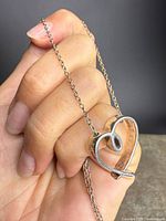 Front view of sterling silver open heart pendant held in hand