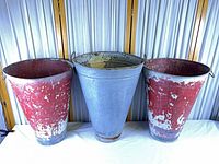 Front view of red distressed tapered metal bucket alongside others for scale