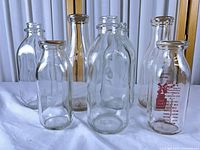 Front view of all seven clear glass milk bottles showing varying heights and one printed red Tops Dairy bottle