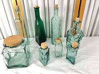 group view of seven green-tinted bottles and jars with corks