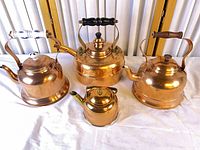 Four copper kettles/teapots grouped on table showing front and side detail