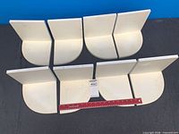 Eight white MDF corner shelves arranged for size reference, ruler visible