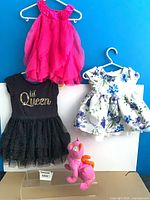 Group shot of three dresses on hangers and plush toy