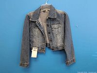 Front view of blue child’s denim jacket on hanger showing overall style and button front