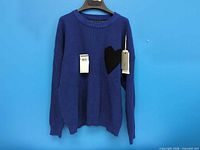 Front view of blue sweater showing tags and black heart patch