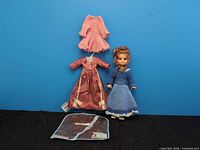 Full lot: doll standing, extra dresses above, storage bag below