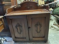 Front view of wooden dry sink cabinet with scroll backsplash and carved doors